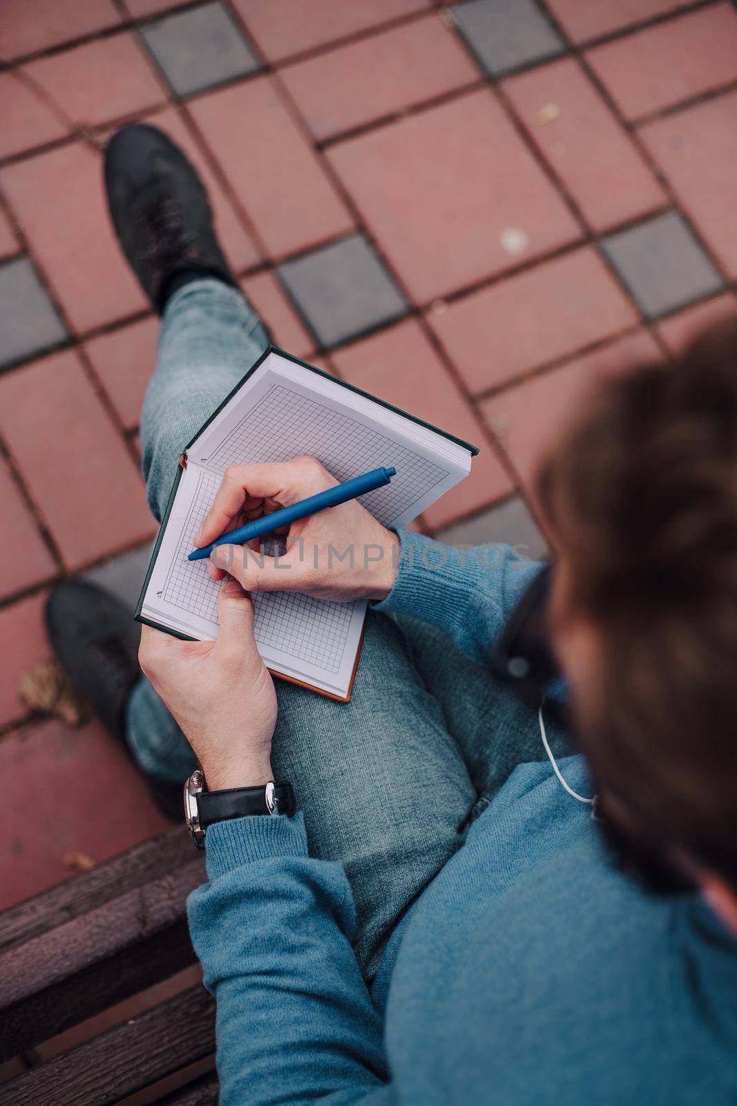 young gay hipster boy notice ideas siting in a park and listen music by headphones