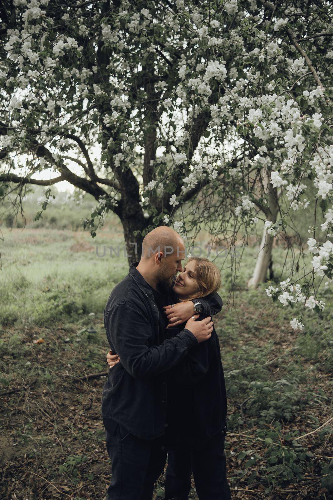 lovers embrace under a flowering tree hiding from the rain