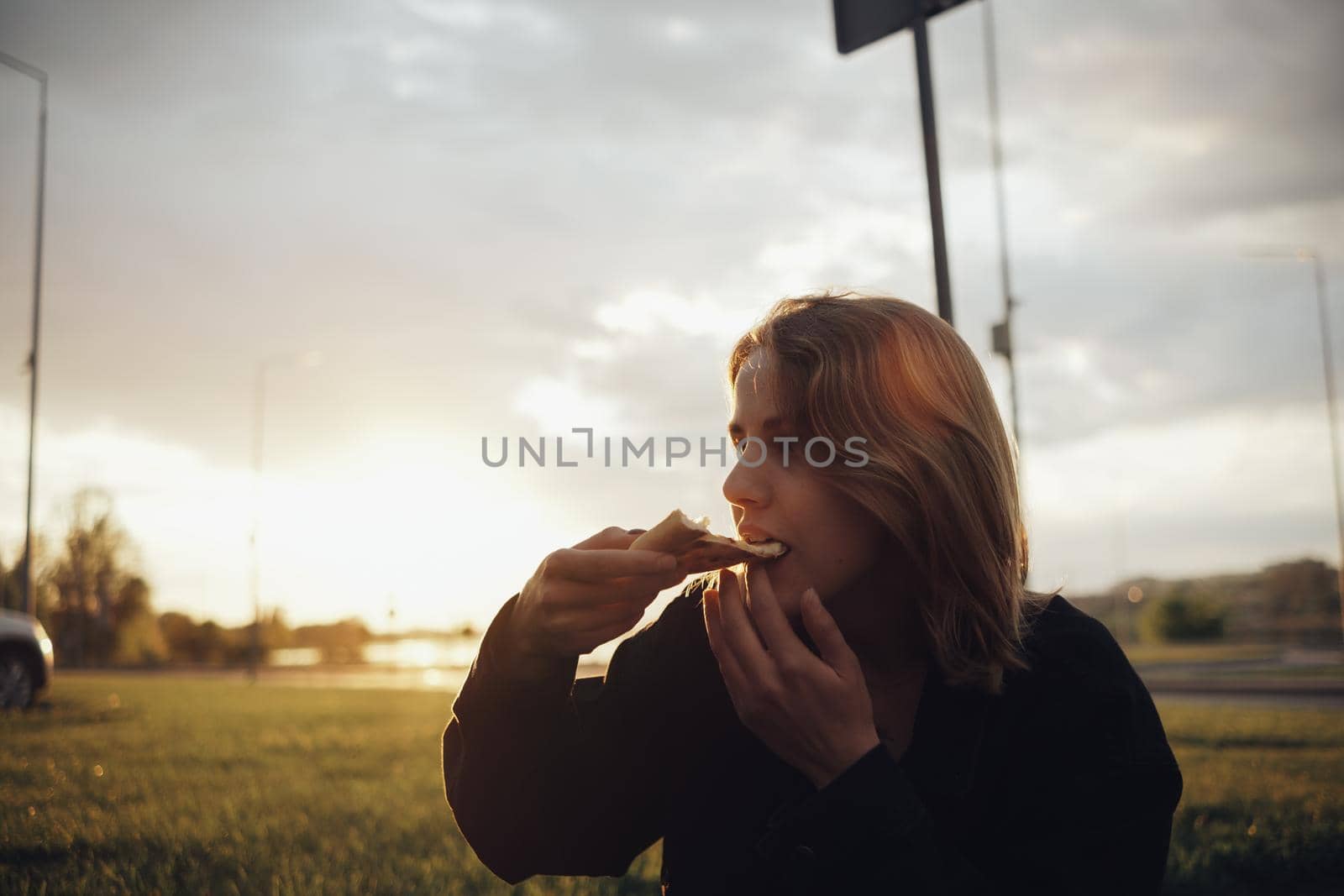 blonde girl eating pizza sitting outside at sunset