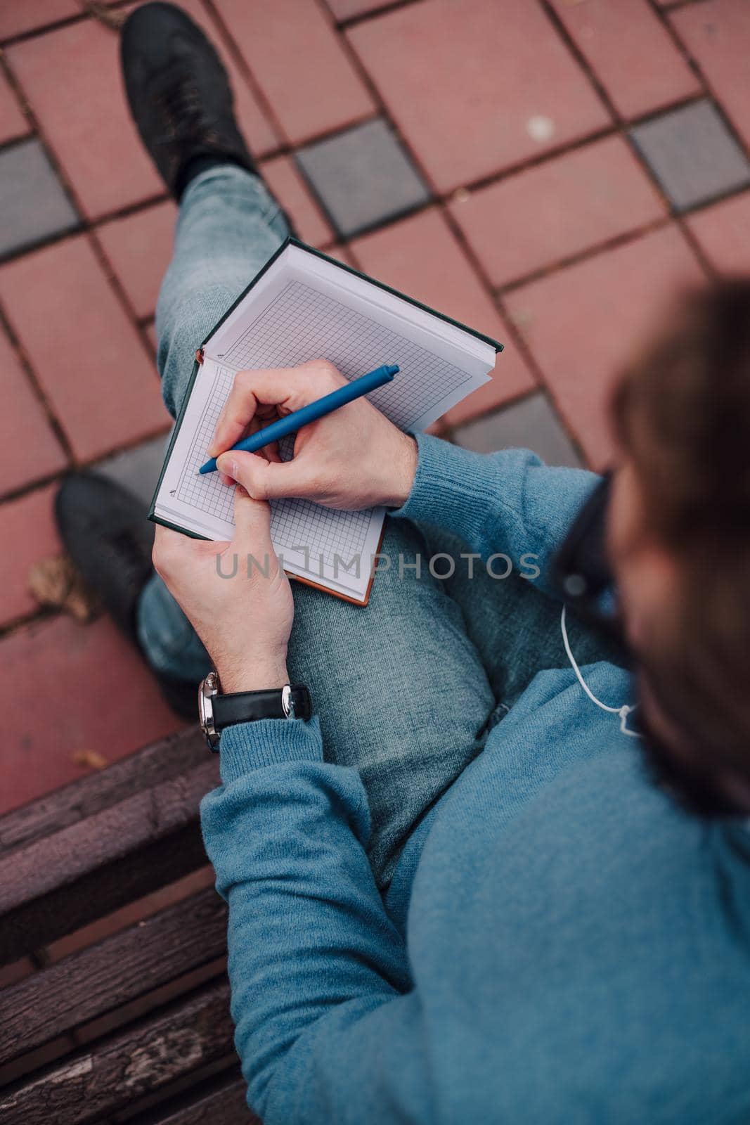 young gay hipster boy notice ideas siting in a park and listen music by headphones