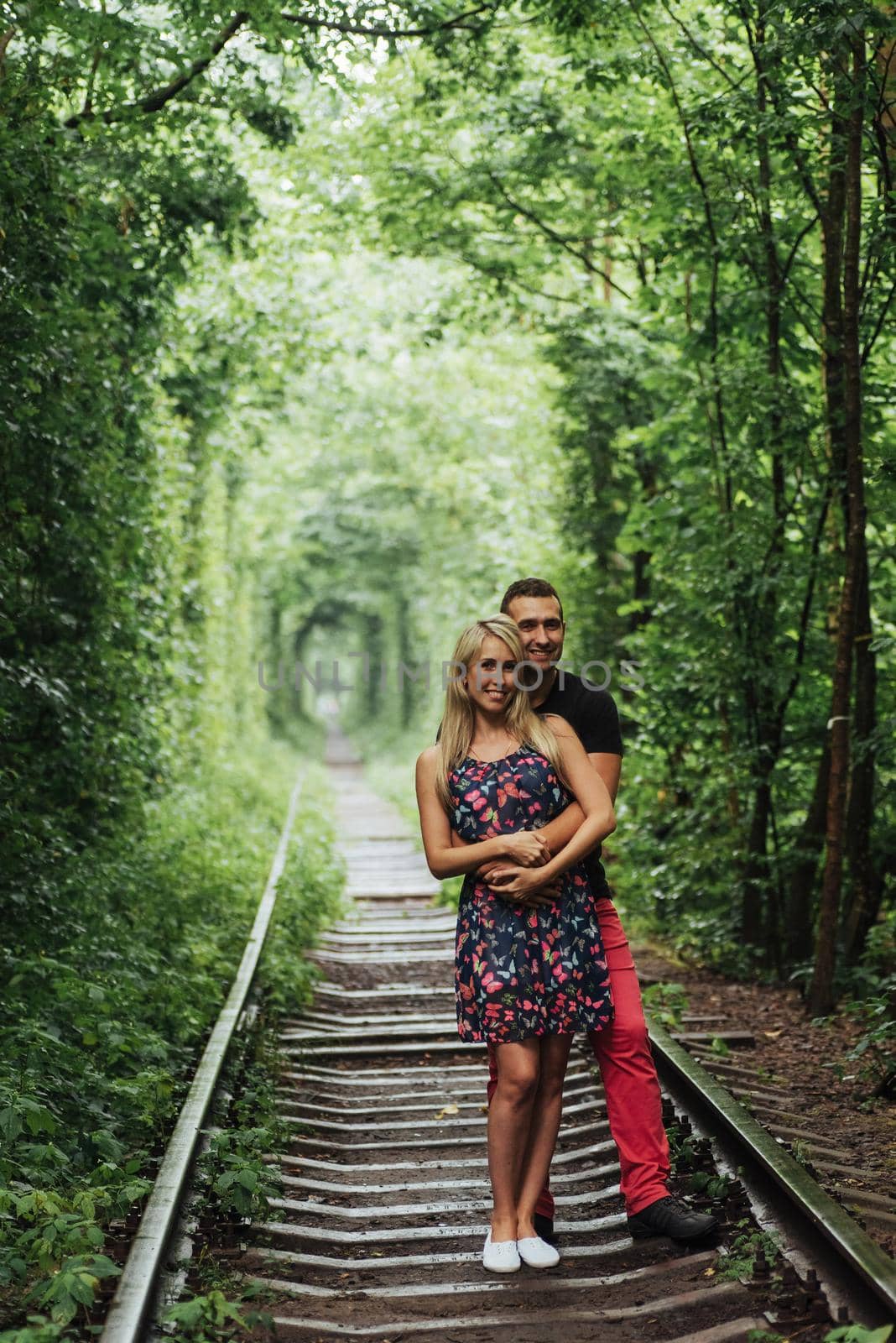 Loving couple in a tunnel of green trees on railroad by Standret