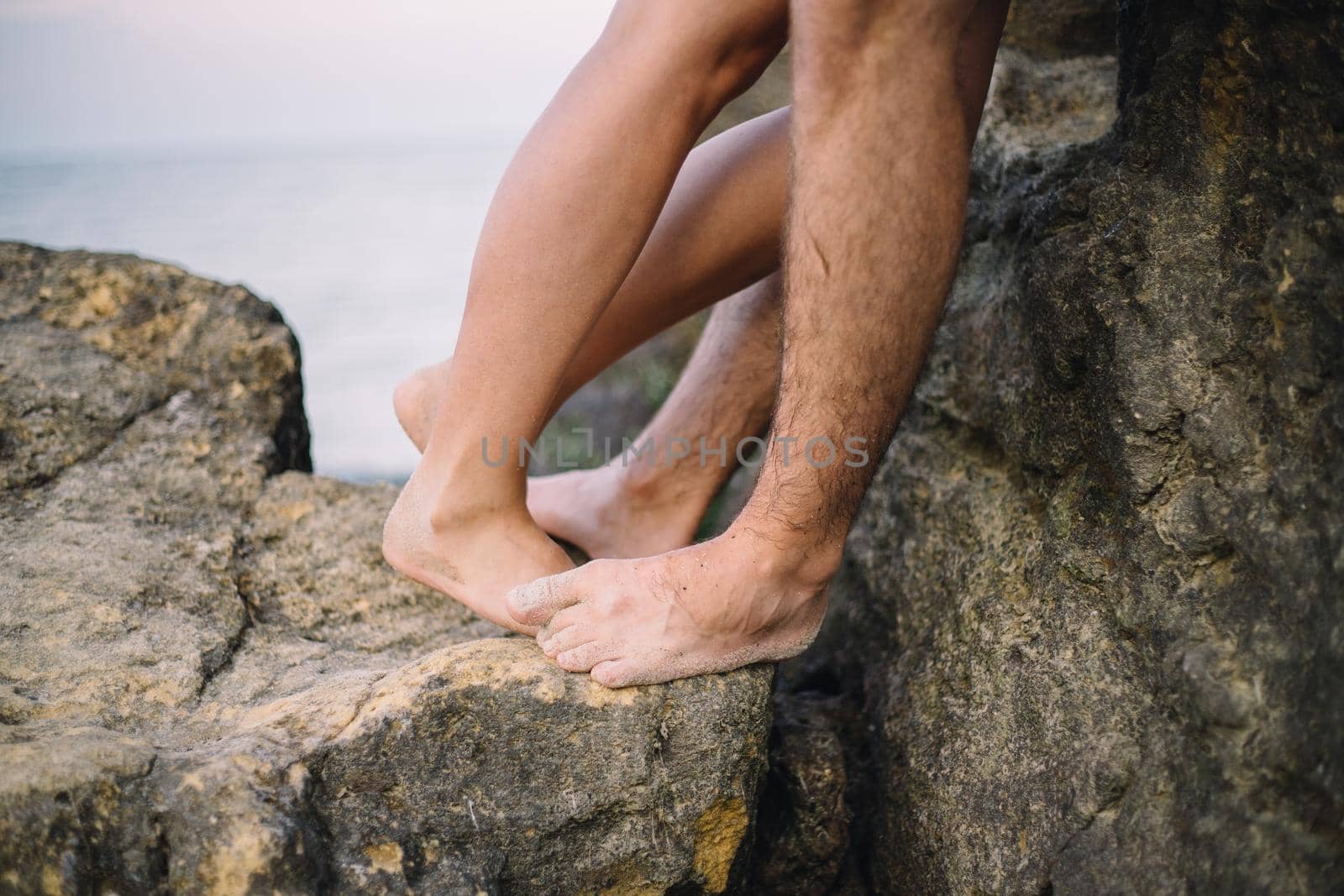 close up legs of kissing couple near the sea on the rocks by Symonenko