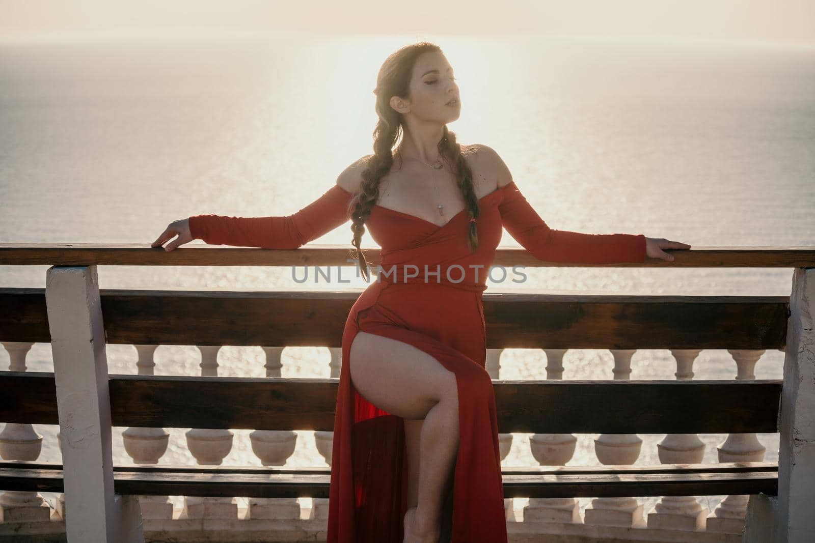 Closeup video portrait of sensual young brunette woman in red dress, happily dancing outdoors isolated on blurry sea background with natural bokeh in soft warm sunset backlight