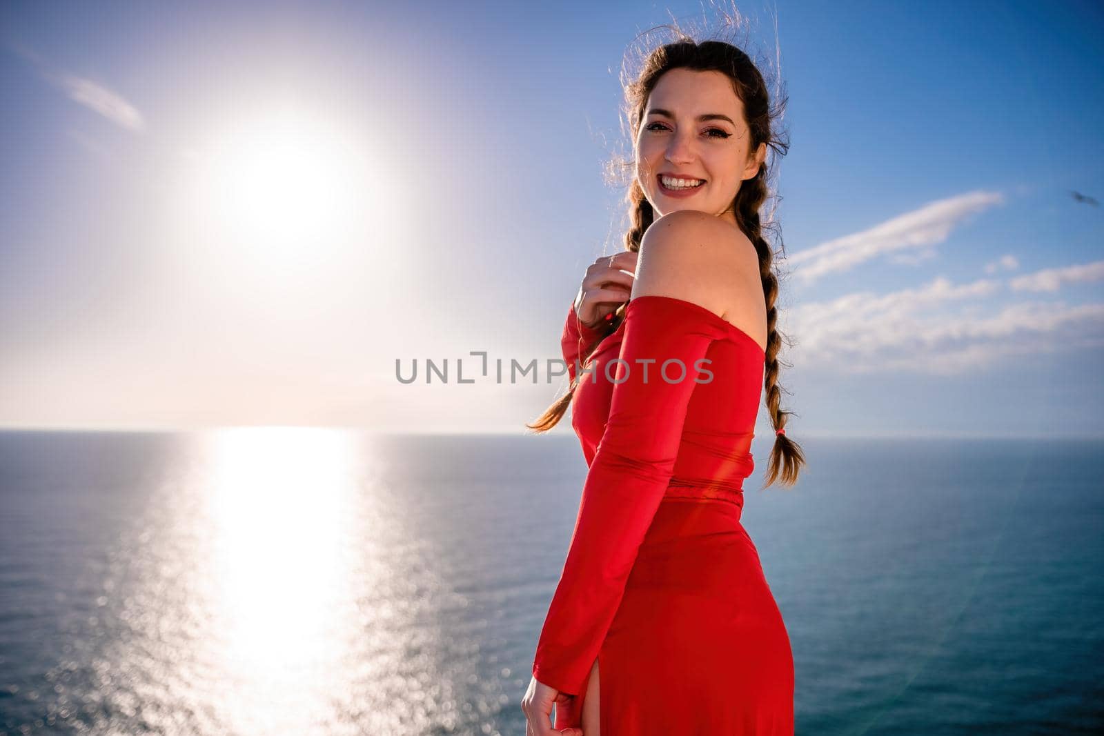 Closeup video portrait of sensual young brunette woman in red dress, happily dancing outdoors isolated on blurry sea background with natural bokeh in soft warm sunset backlight