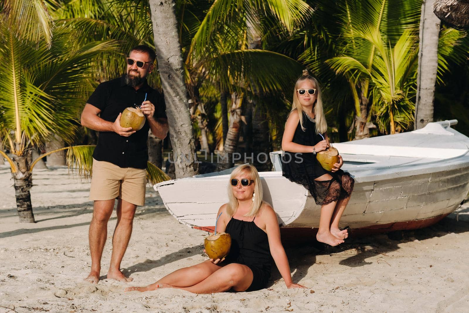 a stylish family in black clothes with coconuts in their hands on the beach of the island of Mauritius.Beautiful family on the island of Mauritius in the Indian ocean by Lobachad