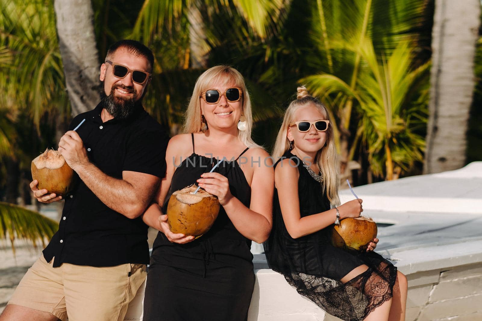 a stylish family in black clothes with coconuts in their hands on the beach of the island of Mauritius.Beautiful family on the island of Mauritius in the Indian ocean by Lobachad