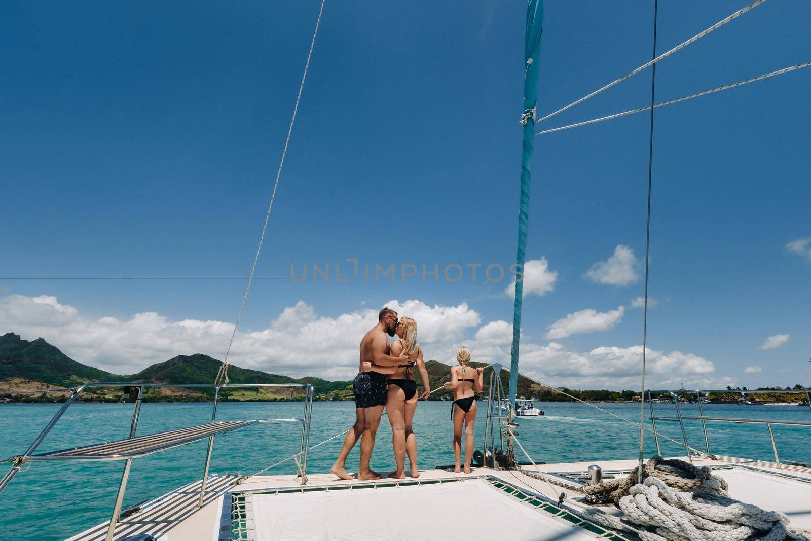 a happy family in swimsuits stands on a catamaran in the Indian Ocean. portrait of a family on a yacht in the coral reef of the island of Mauritius by Lobachad