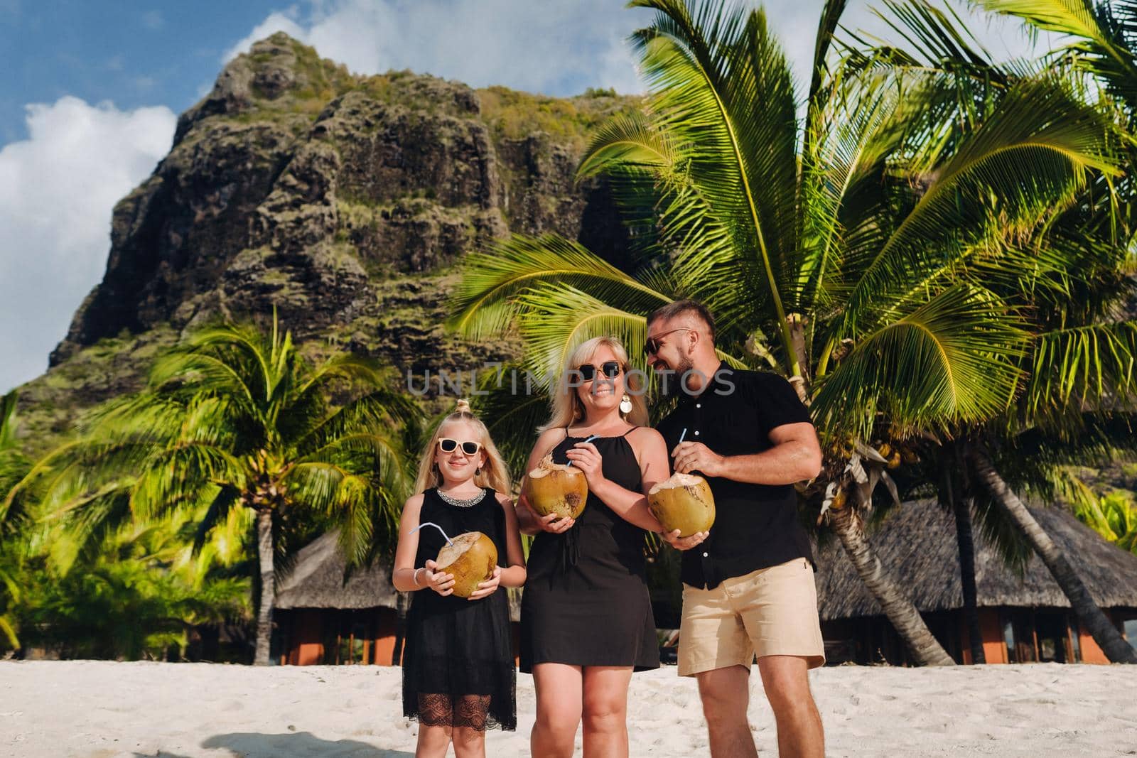 a stylish family in black clothes with coconuts in their hands on the beach of the island of Mauritius.Beautiful family on the island of Mauritius in the Indian ocean.