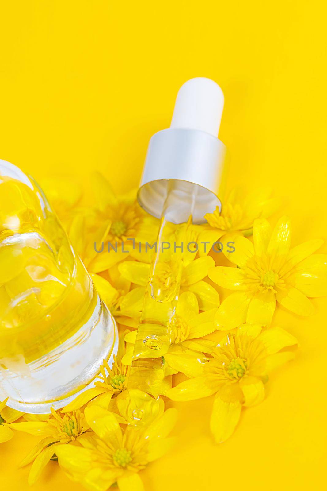 A bottle with a pipette serum on a yellow background surrounded by spring flowers