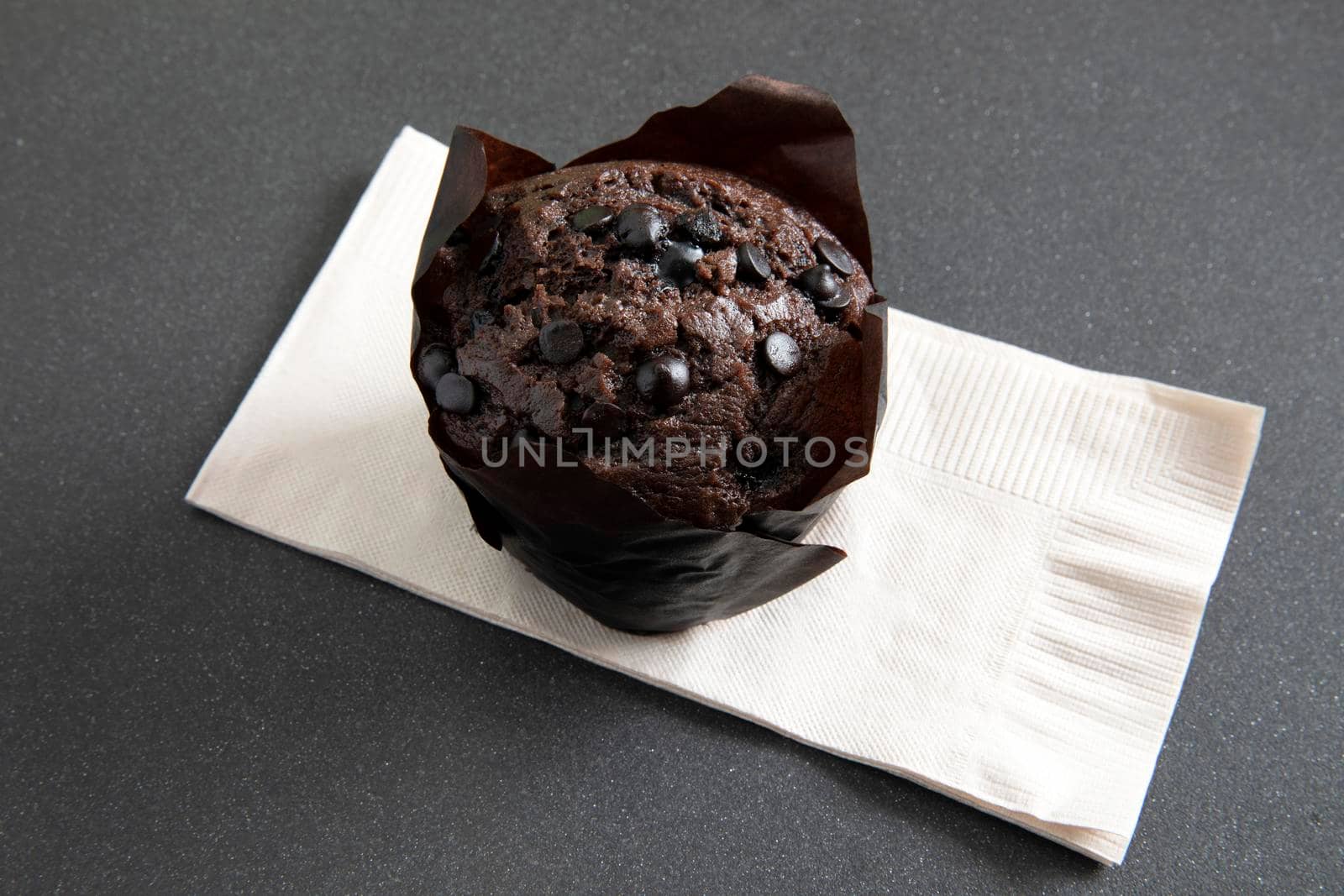 Chocolate muffin in brown paper cup with chocolate pieces on beige paper