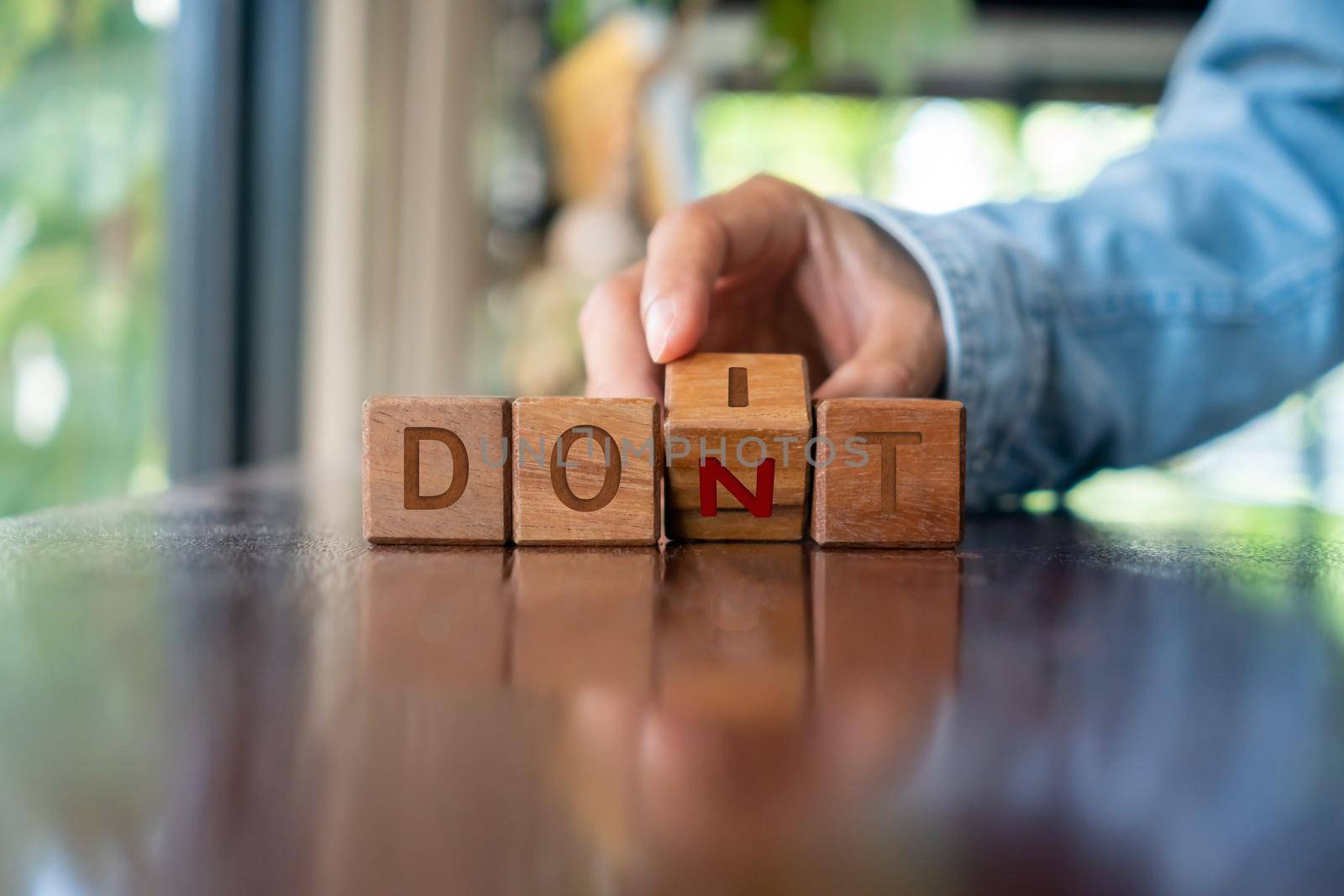 A woman turns a wooden cube with the words do it or don't as a metaphor for making a decision. by Suwant