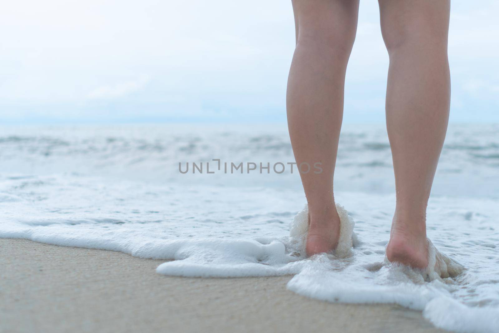 On a sand tropical beach with a blue sky background, a woman's feet walk slowly and relax.