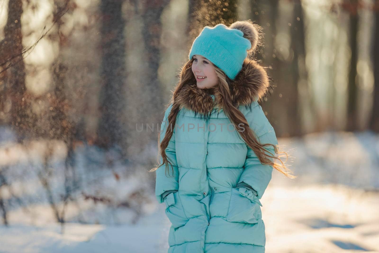 girl in a jacket and hat of turquoise color against the backdrop of a snowy forest