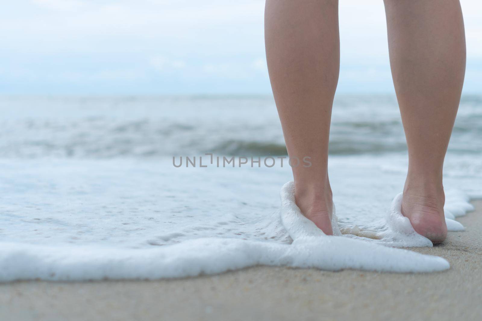 On a sand tropical beach with a blue sky background, a woman's feet walk slowly and relax.