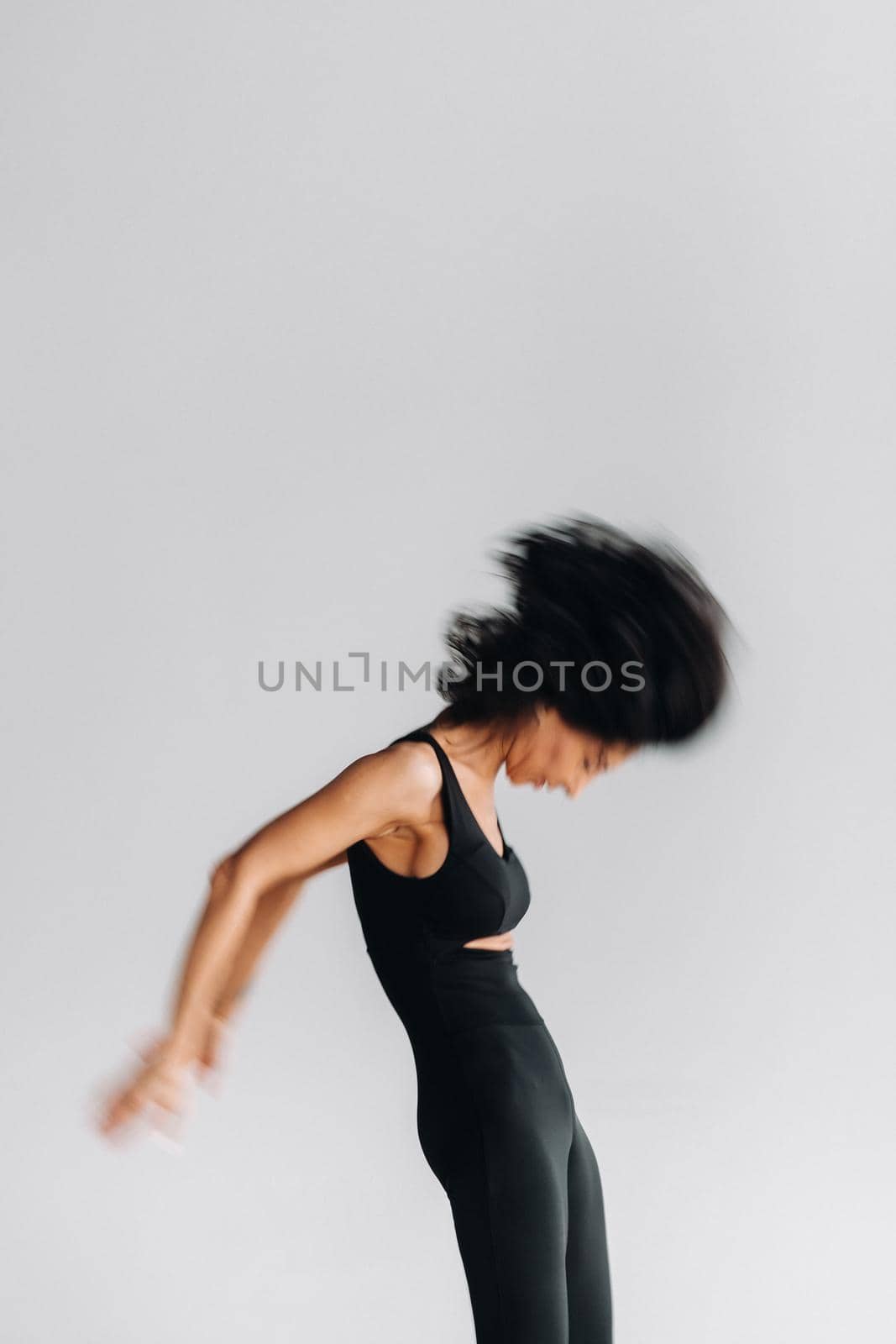 A blurry silhouette of a woman in black sportswear is engaged in dynamic kali meditation in the yoga hall by Lobachad