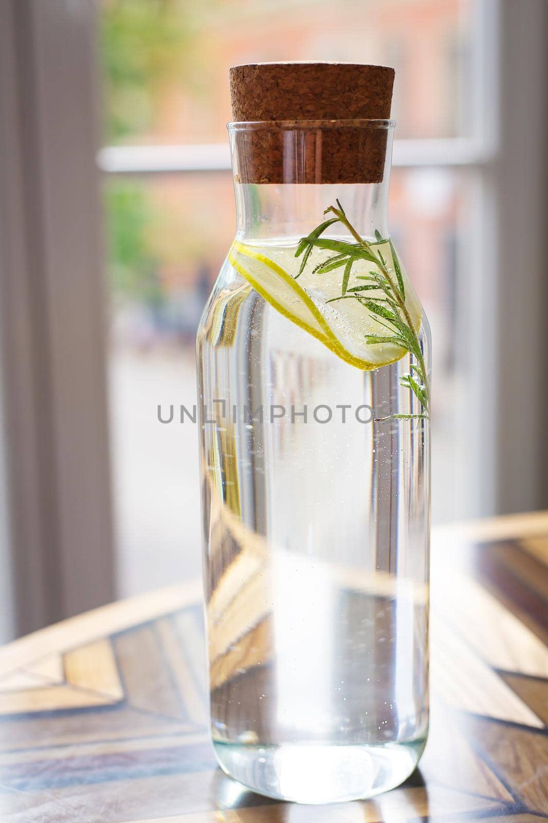 A platter of water with a slice of lemon and a sprig of rosemary. Freshness, a glass of water before lunch, healthy food