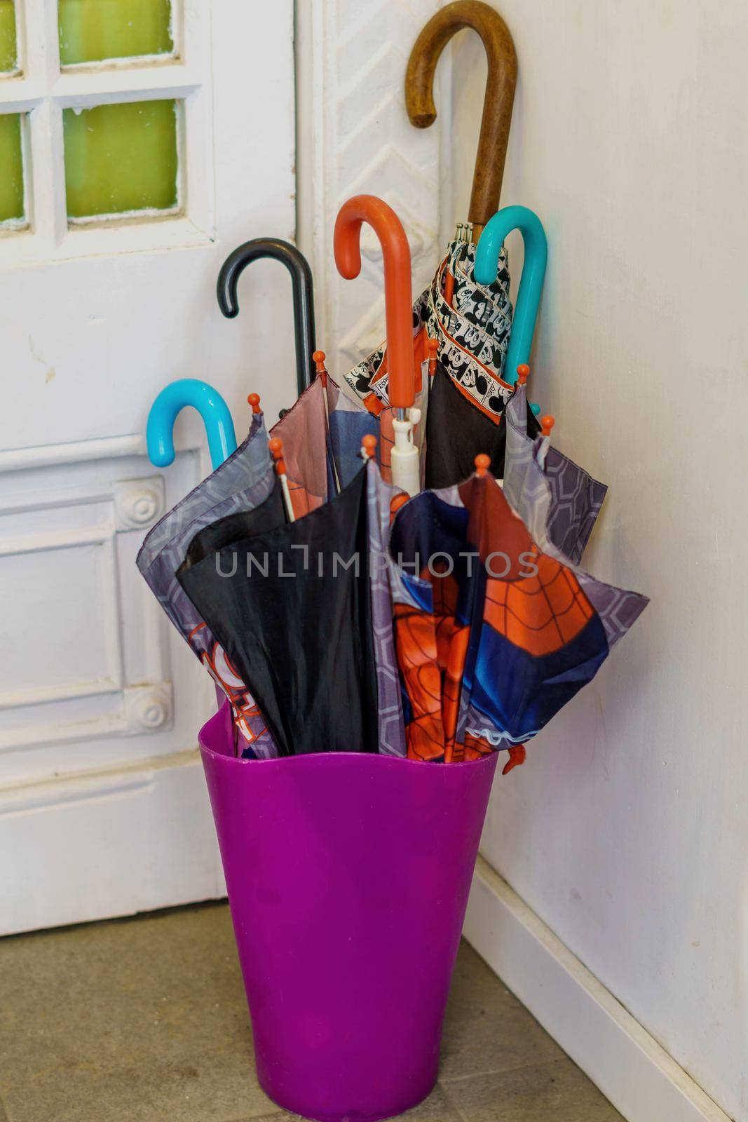 Umbrellas of various colors inside a container at the door of a house. Concept of rain and bad weather