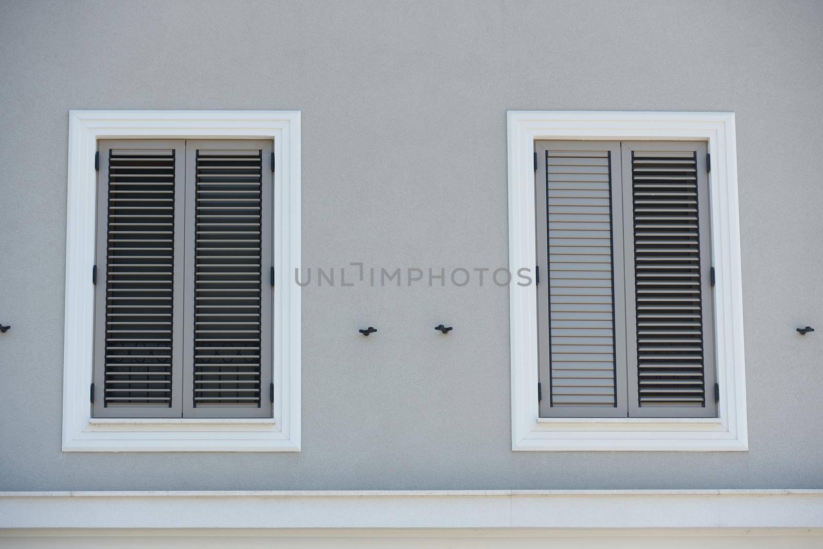 Wall of house with windows and gray closed shutters.