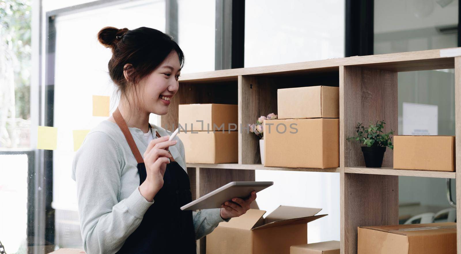 Young beautiful happy asian business woman owner of SME online using laptop receive order from customer with parcel box packaging at her startup home office, online business seller and delivery by wichayada