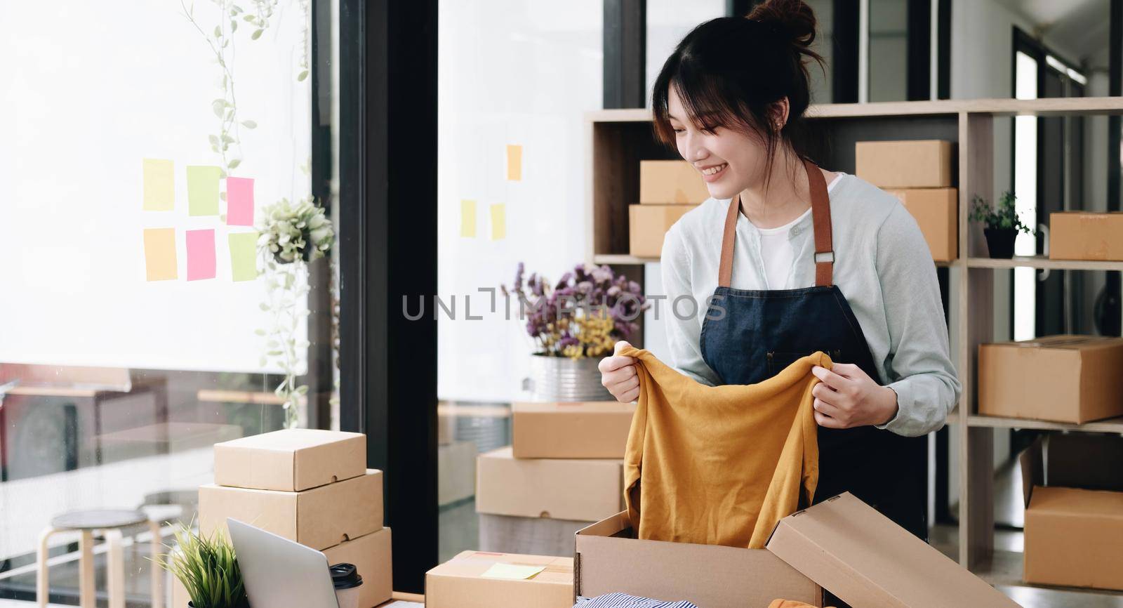 Young beautiful happy asian business woman owner of SME online using laptop receive order from customer with parcel box packaging at her startup home office, online business seller and delivery by wichayada