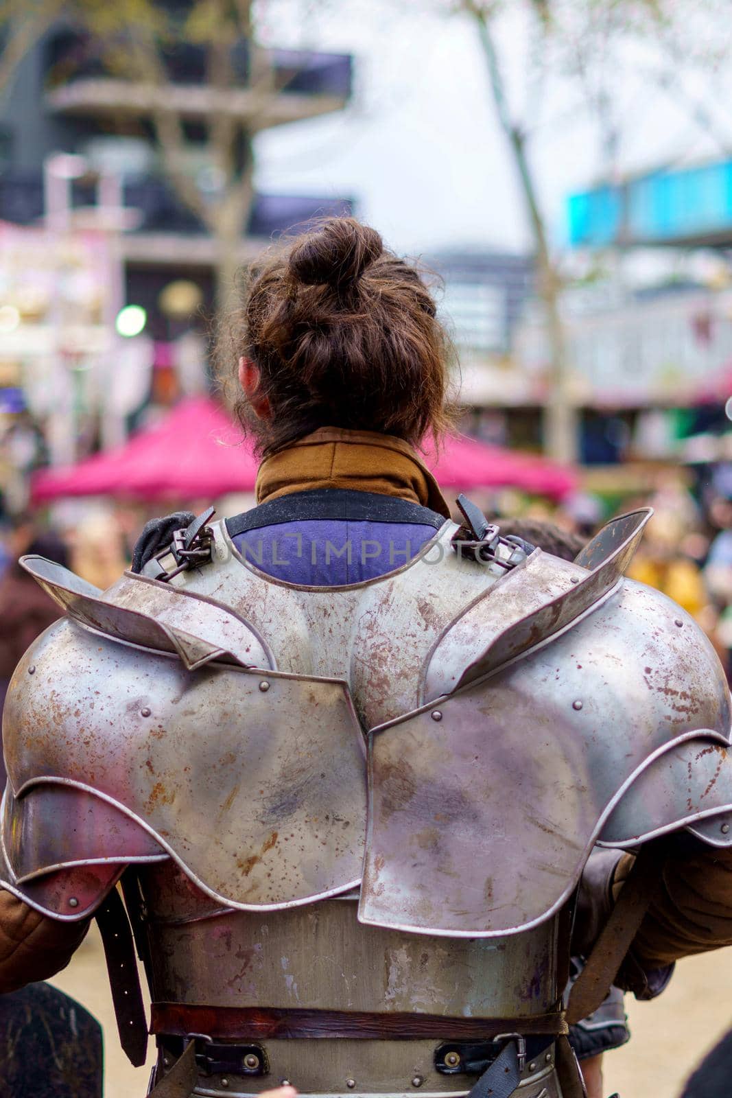 Back of a man dressed in medieval armor during a performance at a popular festival. Close-up view