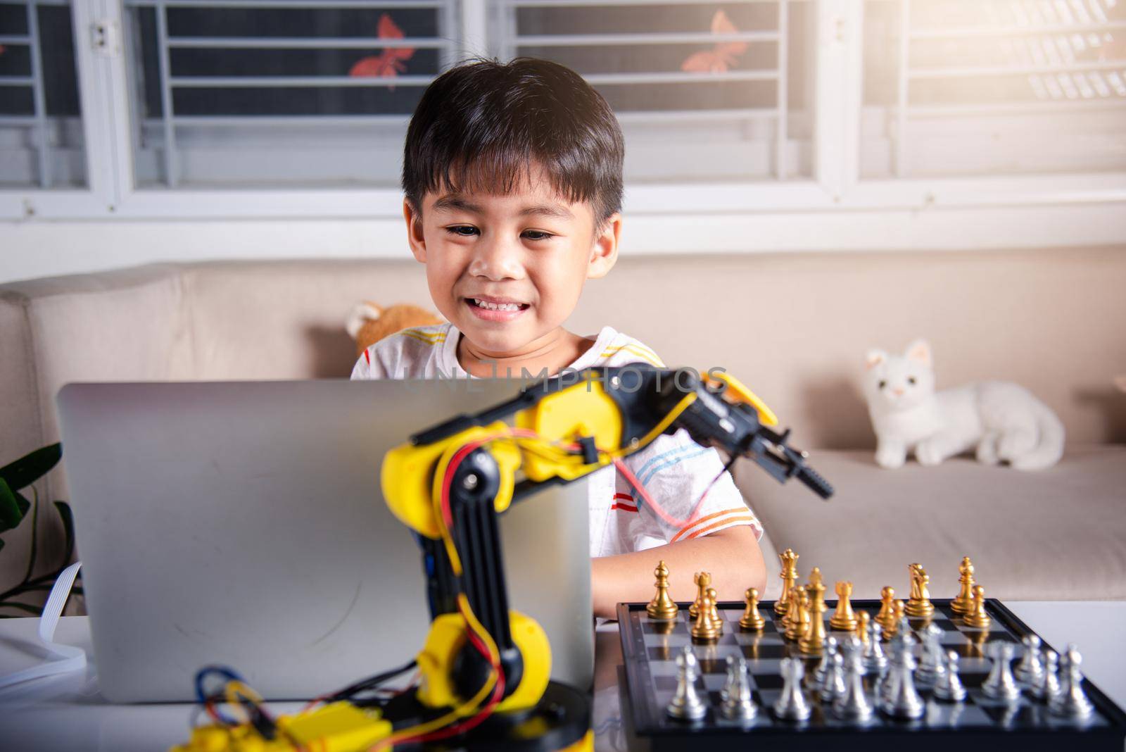 Asian little boy programming code to robot machine arm on laptop for play chess by Sorapop