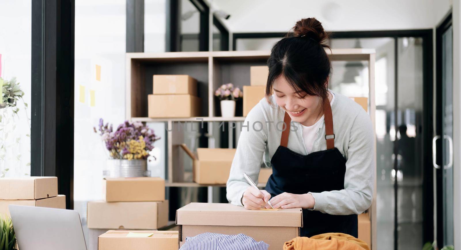 Asian Small business entrepreneur SME writing address on cardboard box at workplace small business entrepreneur SME , working with box at home. by wichayada