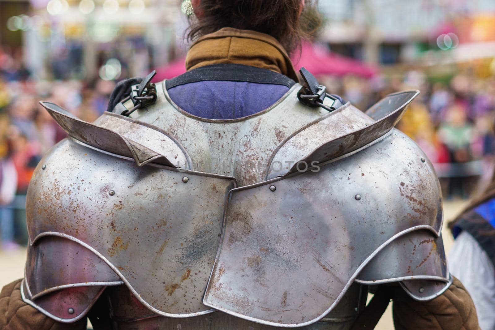 Back of a man dressed in medieval armor during a performance at a popular festival. Close-up view