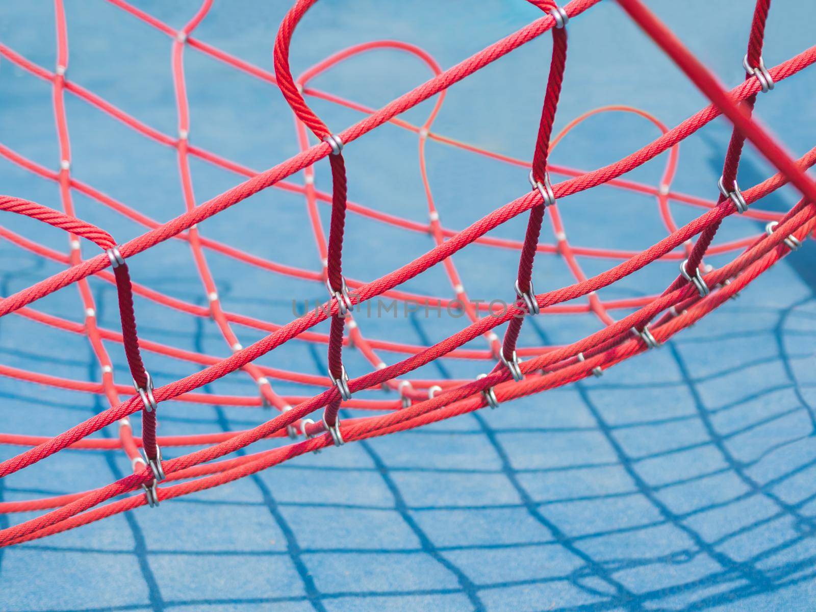 Red net on blue background. Sport equipment on public sportsground in sunny day. Geometrical shadows in sunny day.