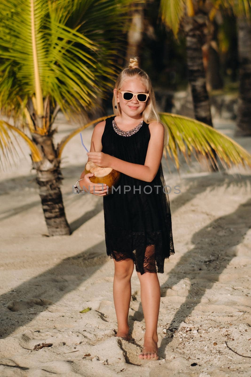 Portrait of a cheerful 9-year-old girl with a coconut cocktail on the background of palm trees on an exotic beach.little Girl with a coconut on the beach of the island of Mauritius by Lobachad