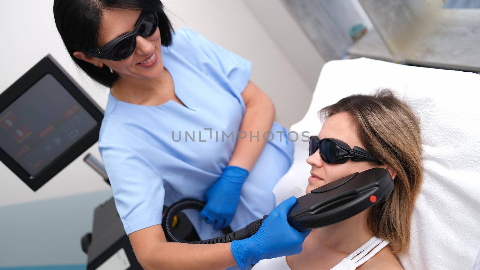 Beautician removing unwanted facial hair of client using laser in beauty salon by kuprevich