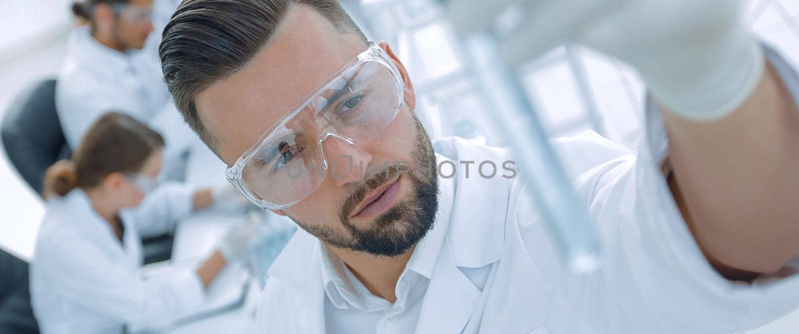 image is blurred. young scientist holding tube with the reagents on the background of the lab.