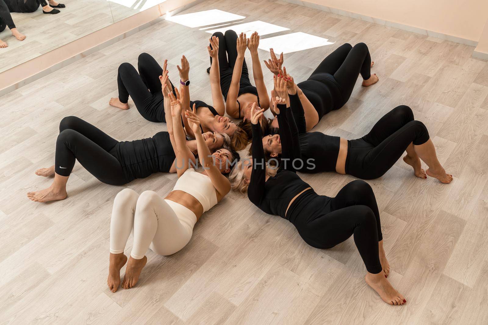 Seven happy women lie on their backs on the floor with their heads pressed together