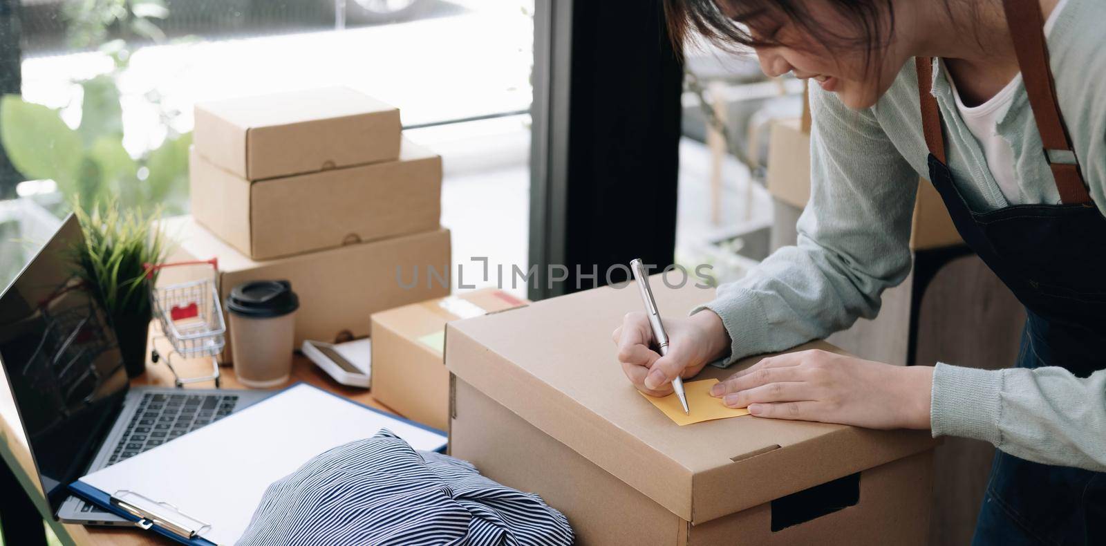 Shipping shopping online ,young start up small business owner writing address on cardboard box at workplace. seller prepare parcel boxs of product for deliver to customer.Online selling or e-commerce by wichayada