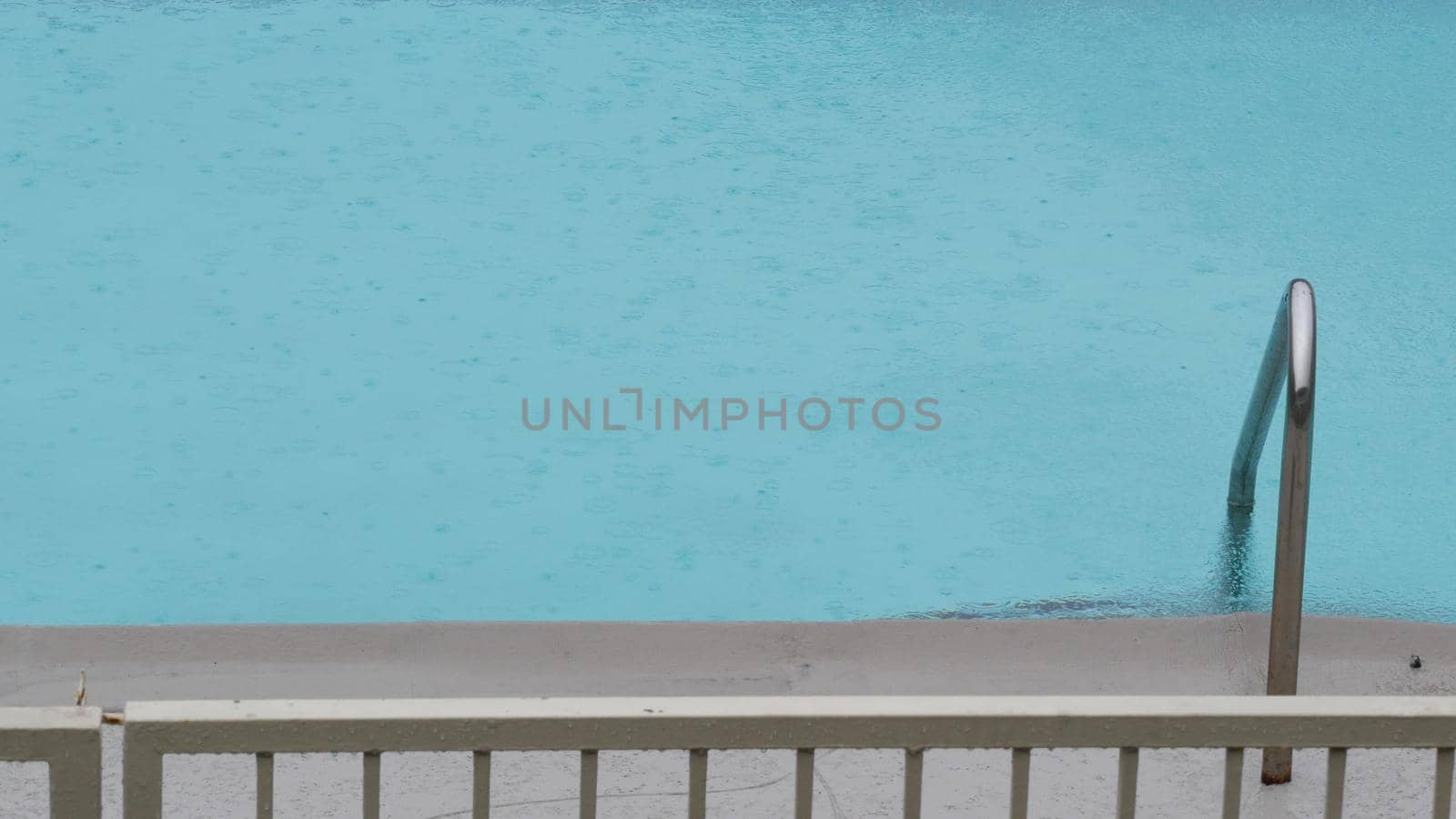 Rain drops falling on water surface of blue swimming pool, rainy day in motel or hotel, California USA. Rainfall on summer vacations, raindrops splashing during monsoon. Seamless looped cinemagraph.