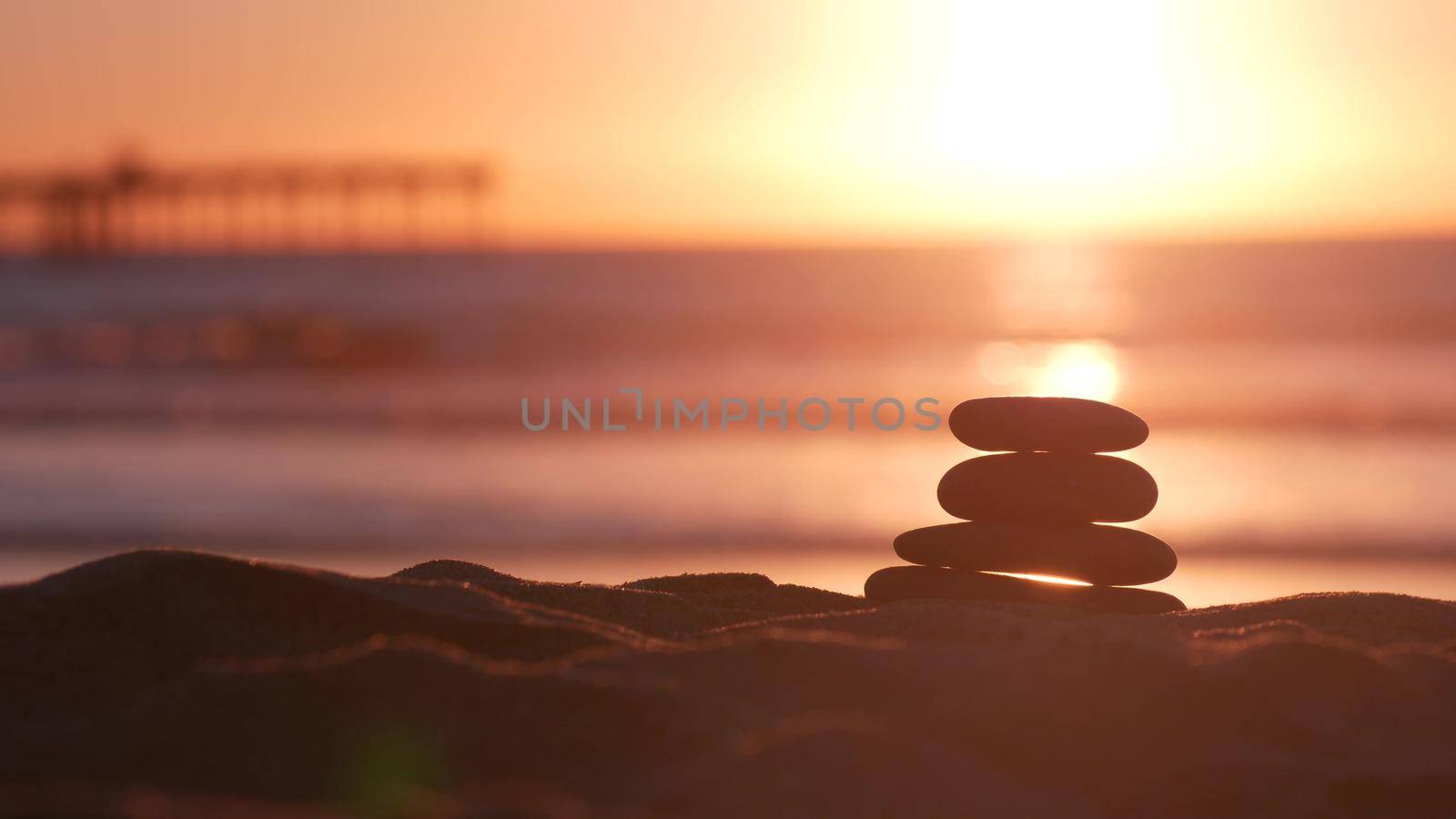 Stack of pebble stones, sandy ocean beach, sunset sky. Rock balancing by water. by DogoraSun