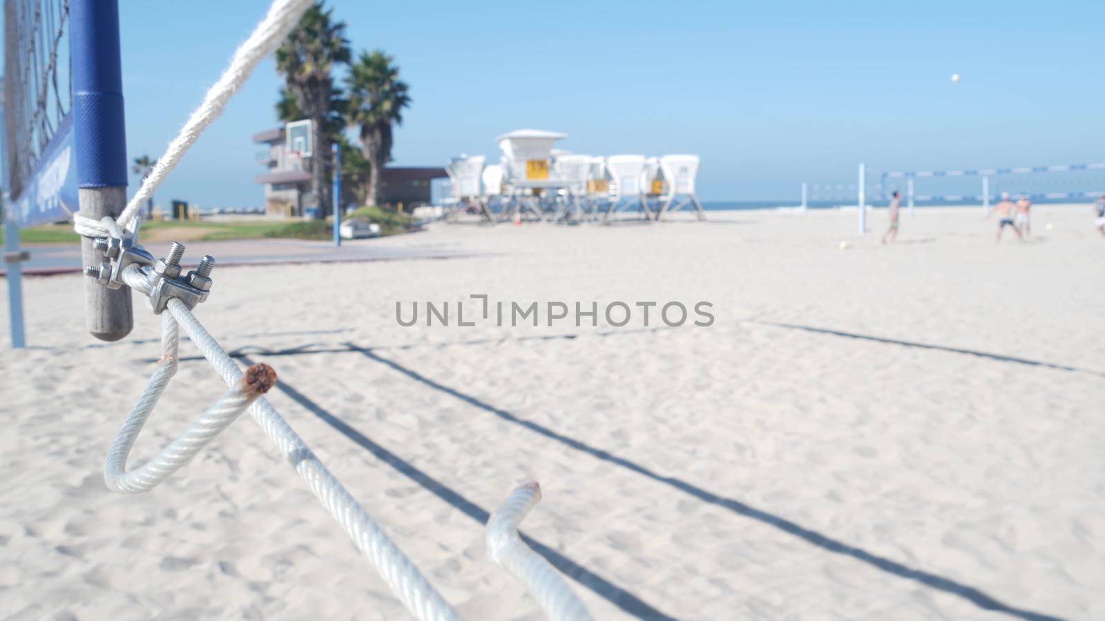 People playing volleyball on beach, lifeguard hut on California coast, USA. Palm trees and outdoor sport field, playground or court on sandy shore. recreational game with net and ball on Mission beach