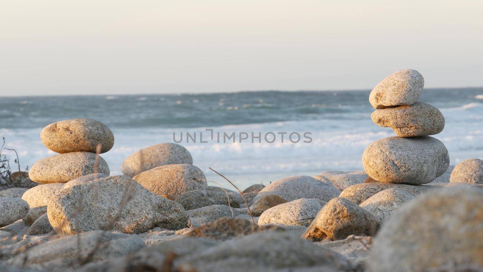 Rock balancing on pebble beach, Monterey 17-mile drive, California coast, USA. Stable pyramid stacks of round stones, sea ocean water waves crashing at sunset. Serenity harmony, calm zen meditation.