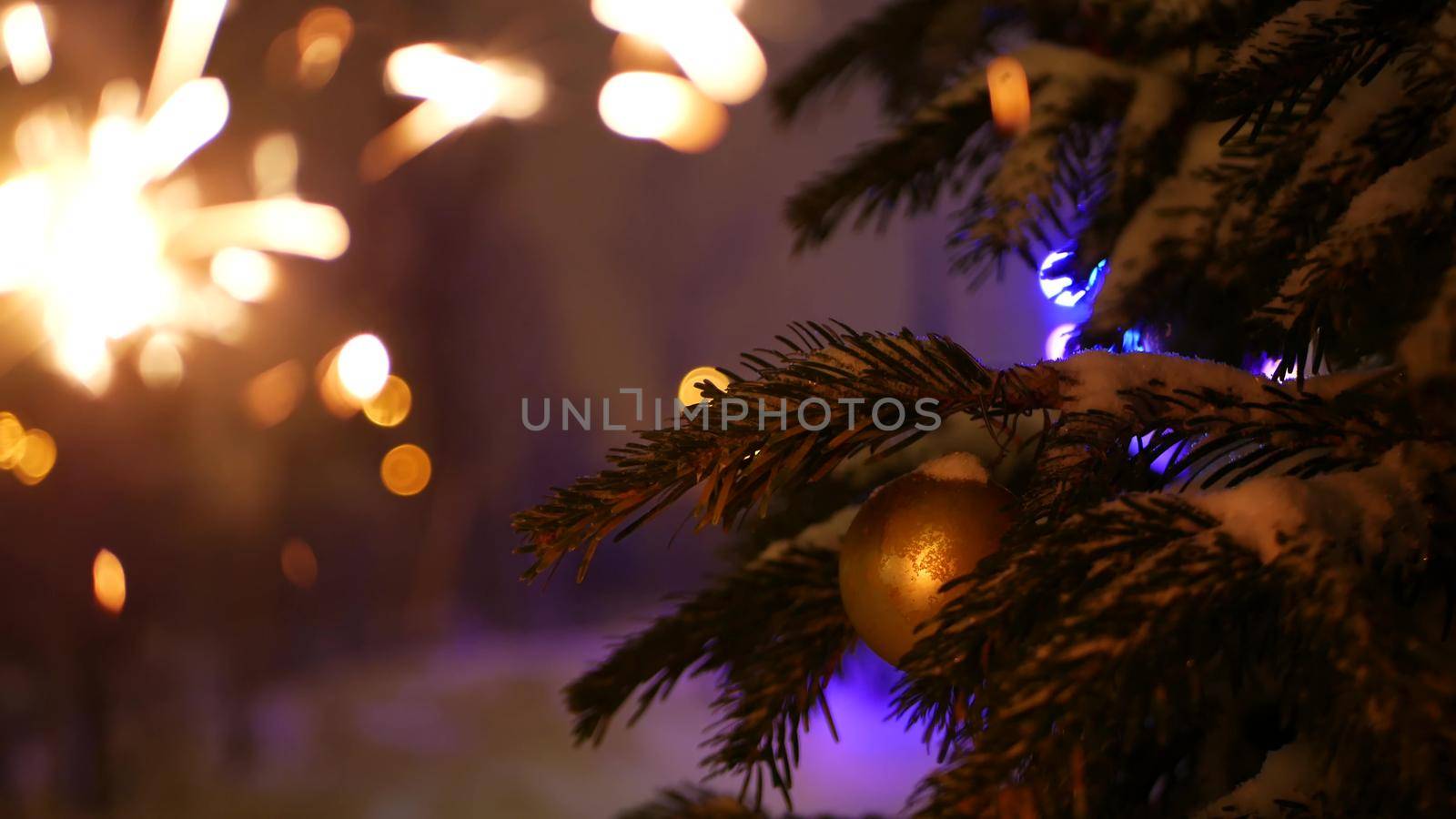 Christmas tree in snow, sparkler firework burning, New Year or Xmas bengal light. Winter holiday magic, sparkles, flakes, golden stars. Spruce, pine or fir in snowflakes. Seamless looped cinemagraph.
