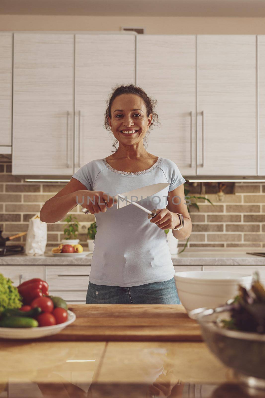 Housewife prepares to cut vegetables for a salad and sharpens a large knife standing in the kitchen