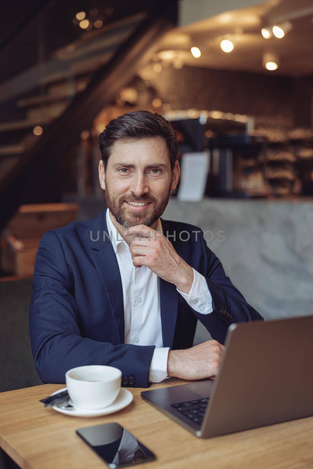 Handsome happy Caucasian businessman sitting at laptop, smiling in cafe. Vertical. Success. Portrait