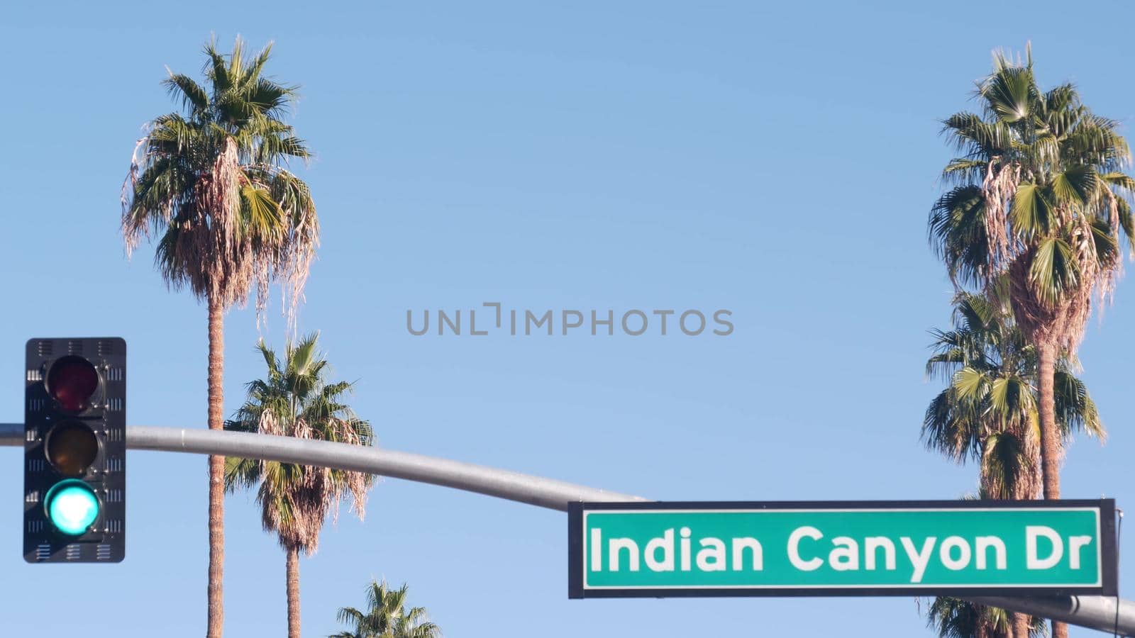 Palm trees and blue sky, Palm Springs resort city near Los Angeles, street road sign, semaphore traffic lights on crossroad. California desert valley summer road trip on car, travel USA. Indian Canyon