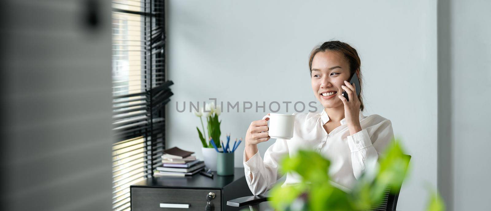 Young asian businesswoman beautiful charming smiling and calling with mobile phone in the office by nateemee