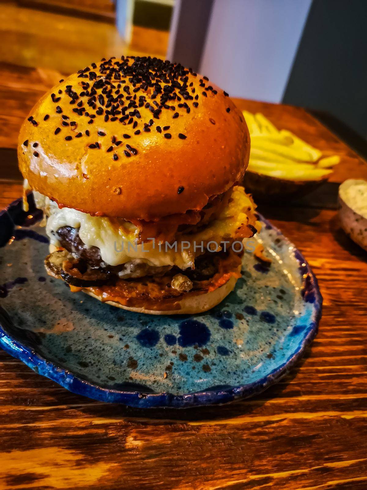 Tall burger with jalapeno peppers and black cumin on a bun lie on a blue plate