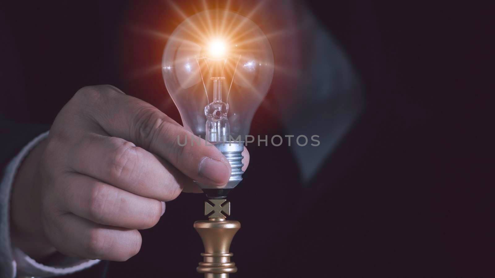 Hand of businessman putting light bulb with fire spark shine glitter on gold king chess new idea with innovation and inspiration, communication with teamwork to victory, strategy concept for success.