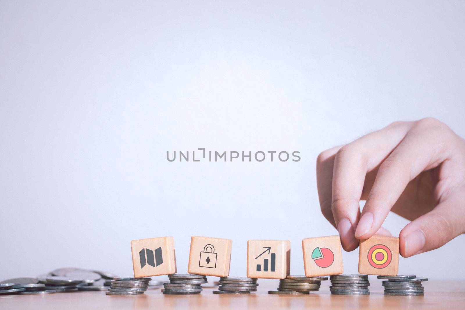 Hand of business strategy or e-commerce taking wooden blocks with target, padlock and graphs icons laying on stack coins or real money  .Business achievement goal,growth success and benefits concept.