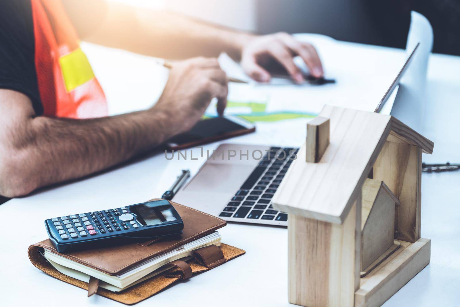 Young man construction worker or engineer working at desk with designer equipment to make interior design at workplace. Real estate business and civil engineering concept.