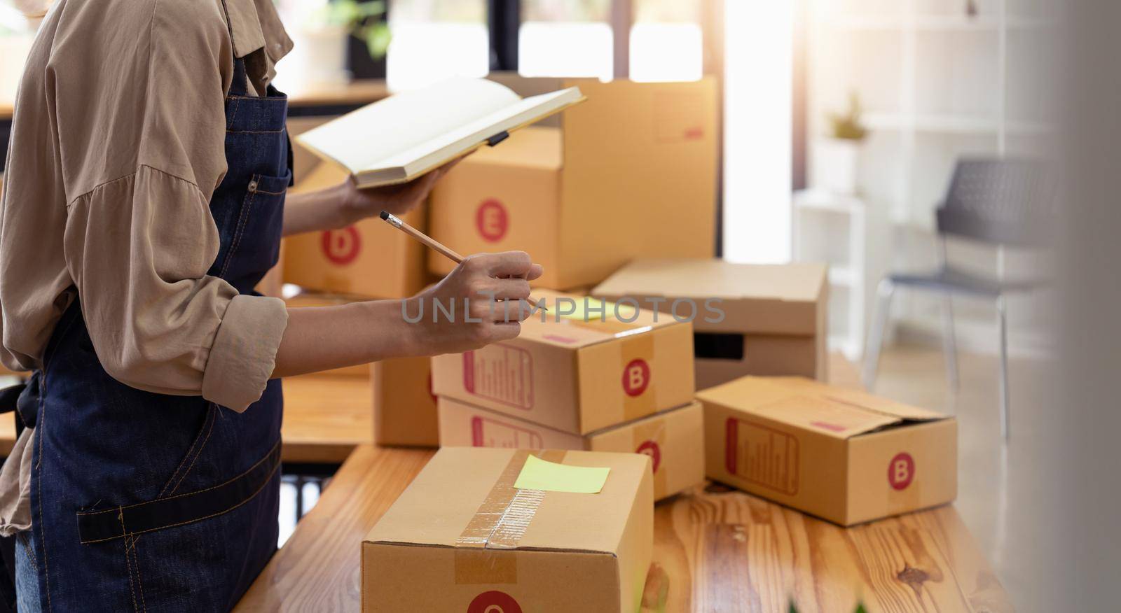 Young asian woman writing address on parcel box at home for delivery order to customer, shipping and logistic, merchant online and seller, business owner or SME, online shopping and e-commerce.