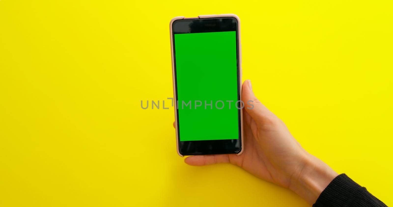 Woman watching content videos on smartphone with Green Mock-up Screen Chroma Key on yellow table background. Phone green screen for product placement. Creative background.