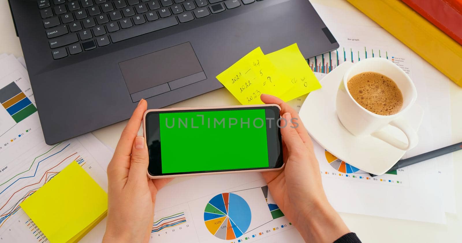 Business woman looking at green screen Mock-up Chroma Key of smartphone sitting at desk in business office, POV. Top view, copy space, worksheet finance graph account chart market plan on desk.